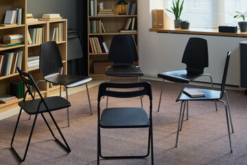 Empty chairs arranged in circle in therapy room suggesting group therapy session setting, books...