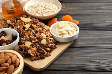 Tasty granola bars with dried fruits and nuts on black wooden table, closeup. Space for text