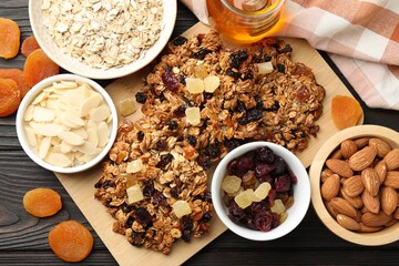 Tasty granola bars with dried fruits and nuts on black wooden table, flat lay