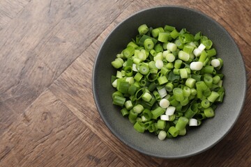 Cut green onion in bowl on wooden table, top view. Space for text