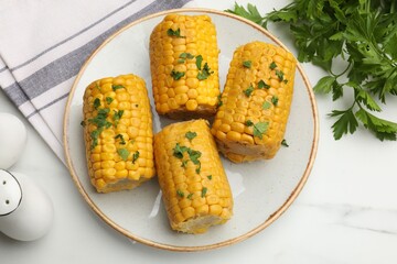 Pieces of boiled corncobs with parsley on white marble table, flat lay