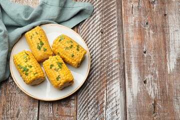 Pieces of boiled corncobs with parsley on wooden table, top view. Space for text