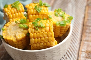 Pieces of boiled corncobs with green onion in bowl on wooden table, closeup