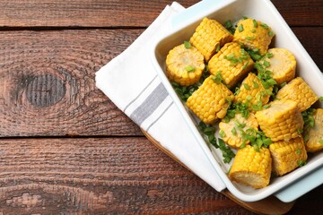 Pieces of boiled corncobs with green onion in baking dish on wooden table, top view. Space for text