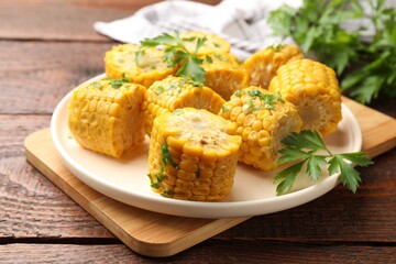 Pieces of boiled corncobs with parsley on wooden table, closeup