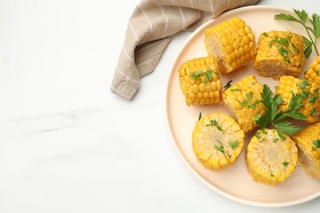 Pieces of boiled corncobs with parsley on white marble table, top view. Space for text