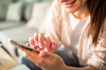 Young adult woman smiling while texting on smartphone at home
