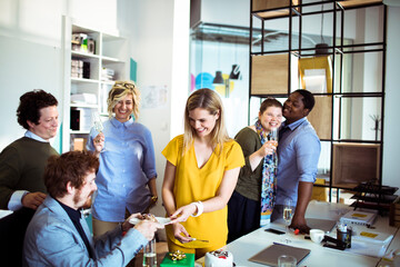 Happy adult coworkers celebrating birthday with cake in modern office