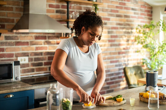 Pregnant adult woman focused while making fresh juice at home kitchen