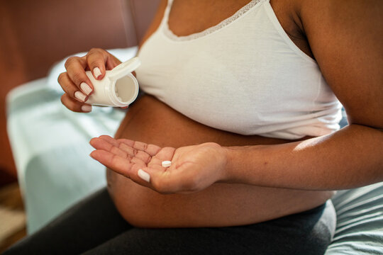 Adult pregnant woman taking prenatal vitamins at home, calm