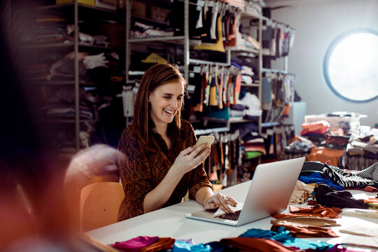 Adult woman laughing, managing online shop in fashion studio