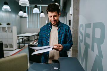 Office worker reviewing printed documents in modern workspace while smiling during a productive day