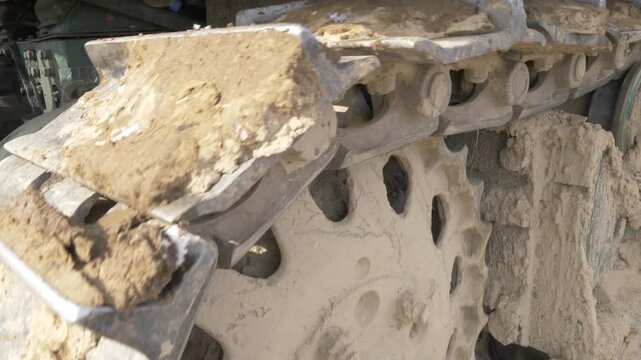Close-up of bulldozer caterpillar tracks moving through mud and snow.