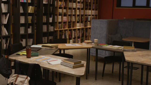 No people shot of library study area featuring shared table with coursebooks, stationery and eco friendly thermal cups, workspace arranged for English language training course session