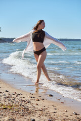 Young woman enjoying Baltic Sea beach with open arms under clear sky