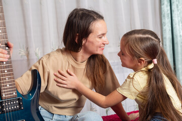 girl learns to play the guitar with her mother