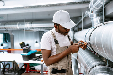 Young technician repairs ventilation system in modern workshop space during daylight hours