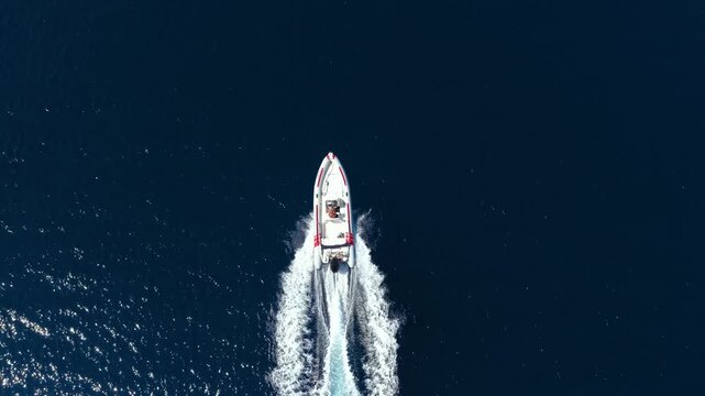 Aerial overhead zoom out rocket view of a RIB motorboat cruising over the ocean with speed