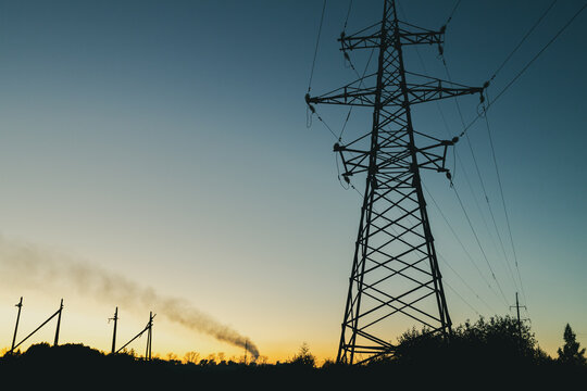 a power line pole against the sky at sunset, smoke from a chimney and old poles