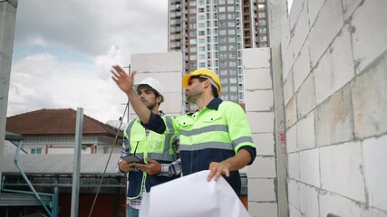 Two engineers wearing safety gear review construction plans while observing progress at an active building site. The scene reflects teamwork, professional planning, and structural development in an ur