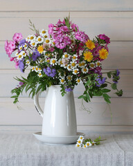 Wildflower bouquet standing in white ceramic pitcher on linen