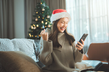 Happy woman celebrating Christmas moment while checking smartphone indoors, joyful holiday...
