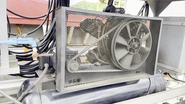 air compressor operating on the deck of a cargo ship. Visible rotating elements, cooling fan and drive belts in motion. Marine compressor supplies compressed air pneumatic tools during ship operations