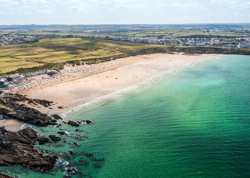 Aerial view of a sun-kissed beach teeming with people, where golden sands meet the turquoise sea, framed by rugged cliffs and the town of Newquay, Newquay, England, United Kingdom.