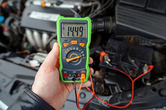 Man with multimeter testing alternator charge level on car battery while engine is idling, 14.5 volts, good charge. Inspection before winter season. Proper voltage, electrical system performance