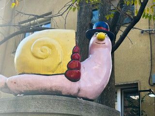 Whimsical snail sculpture with hat beside urban building and tree. Playful outdoor art, colorful street decoration, nostalgic charm and cheerful city atmosphere. © satura_