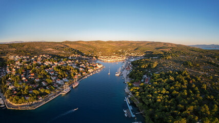 Aerial view of the harbor where the turquoise sea meets the quaint town nestled amidst lush, green hills under a clear sky, Milna, Split-Dalmatia County, Croatia.