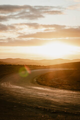 Vertical image of an empty mountain road between the hills of the outback outdoor during a golden sunset with sun flare in Flinders Ranges in Australia with space for text.