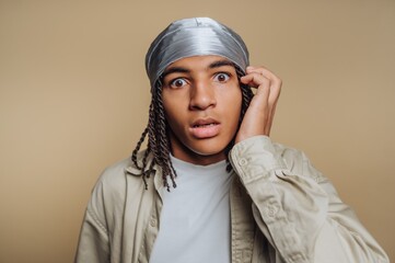 Young person with a surprised expression, wearing a silver headscarf and casual clothing, against a...