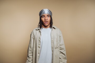 Young person with surprised expression wearing a durag and casual clothing against a beige background.