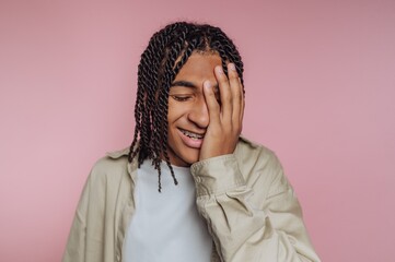 Smiling young person with braided hair covering face, pink background.