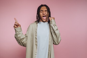 Young person with braided hair singing passionately against a pink background.