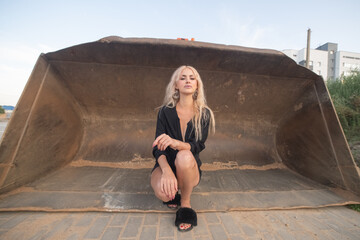 Young woman with blonde hair stands confidently on construction site, wearing casual outfit, surrounded by building materials, showcasing strength and determination in a dynamic outdoor environment