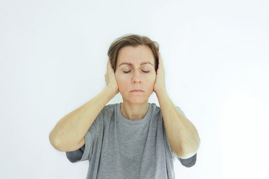 Woman covering her ears with hands to block noise during a migraine attack. Represents sound sensitivity episode, phonophobia symptom, sensory overload protection, and acoustic trigger avoidance.