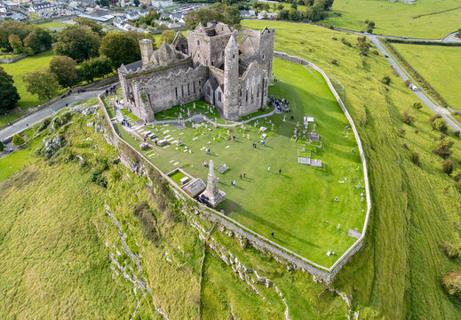 Aerial view of the Rock of Cashel, a historic site with medieval architecture rising dramatically from a grassy hill, casting shadows across the ancient stone, Cashel, County Tipperary, Ireland.