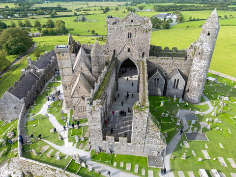 Aerial view of the Rock of Cashel's majestic ruins rise against the green fields, ancient stone contrasting the vibrant landscape, Cashel, County Tipperary, Ireland.