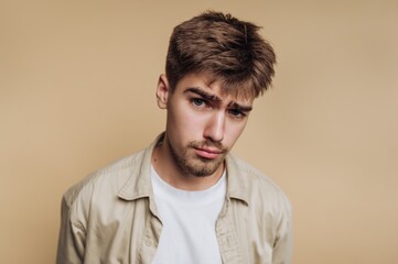 Young man with a puzzled expression against a beige background.