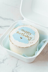 Cute little bento cake with a happy birthday text and blue cream smears in the white gift box on the white marble background