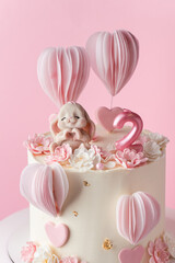 Beautiful birthday cake for a little 2 year old baby girl with a cute chocolate figurine of bunny on the pink background