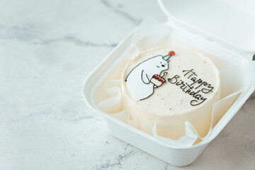Cute bento cake with funny white bear holding a festive cake with a candle drawing. Birthday cake in a white gift box on the white marble background