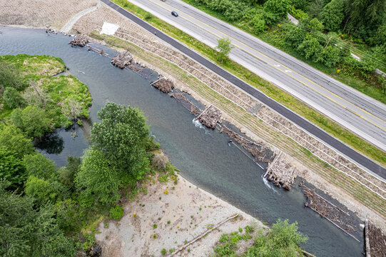 Aerial view of the Cedar River flowing gently, with log structures placed to guide the water, alongside a highway and lush green trees, Renton, Washington, United States.