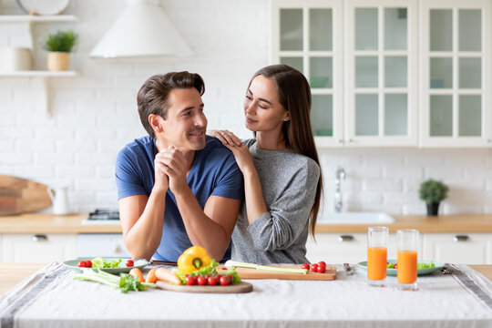 Smiling man in a blue shirt is sitting at a kitchen table with a woman in a gray shirt.