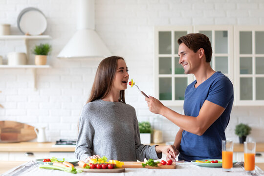 Smiling man in a blue shirt is sitting at a kitchen table with a woman in a gray shirt. Happy expression.