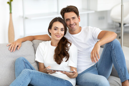 Man and woman are sitting on a gray couch, smiling at each other.