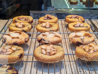 Fresh artisan cookies displayed on a metal rack in a pastry shop window, featuring nut toppings, caramel centers and golden baked texture in a traditional French bakery