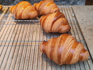 Fresh golden croissants displayed on a bakery rack, showcasing flaky layers, glossy crust and traditional French pastry craftsmanship in a shop window in Nice